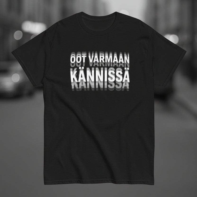 Mustan tekstipaidan etupuolella on painatus 'OOT VARMAAN KANNISSA' selkeällä tyylillä