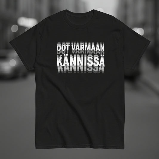 Mustan tekstipaidan etupuolella on painatus 'OOT VARMAAN KANNISSA' selkeällä tyylillä